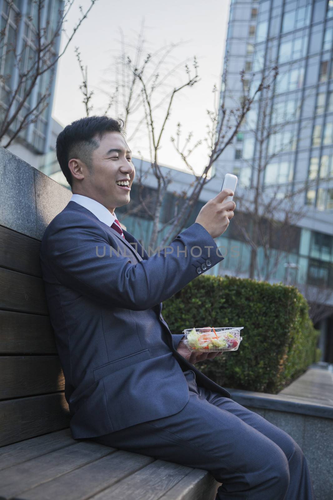 Smiling businessman on lunch texting on his mobile phone outdoors by XiXinXing