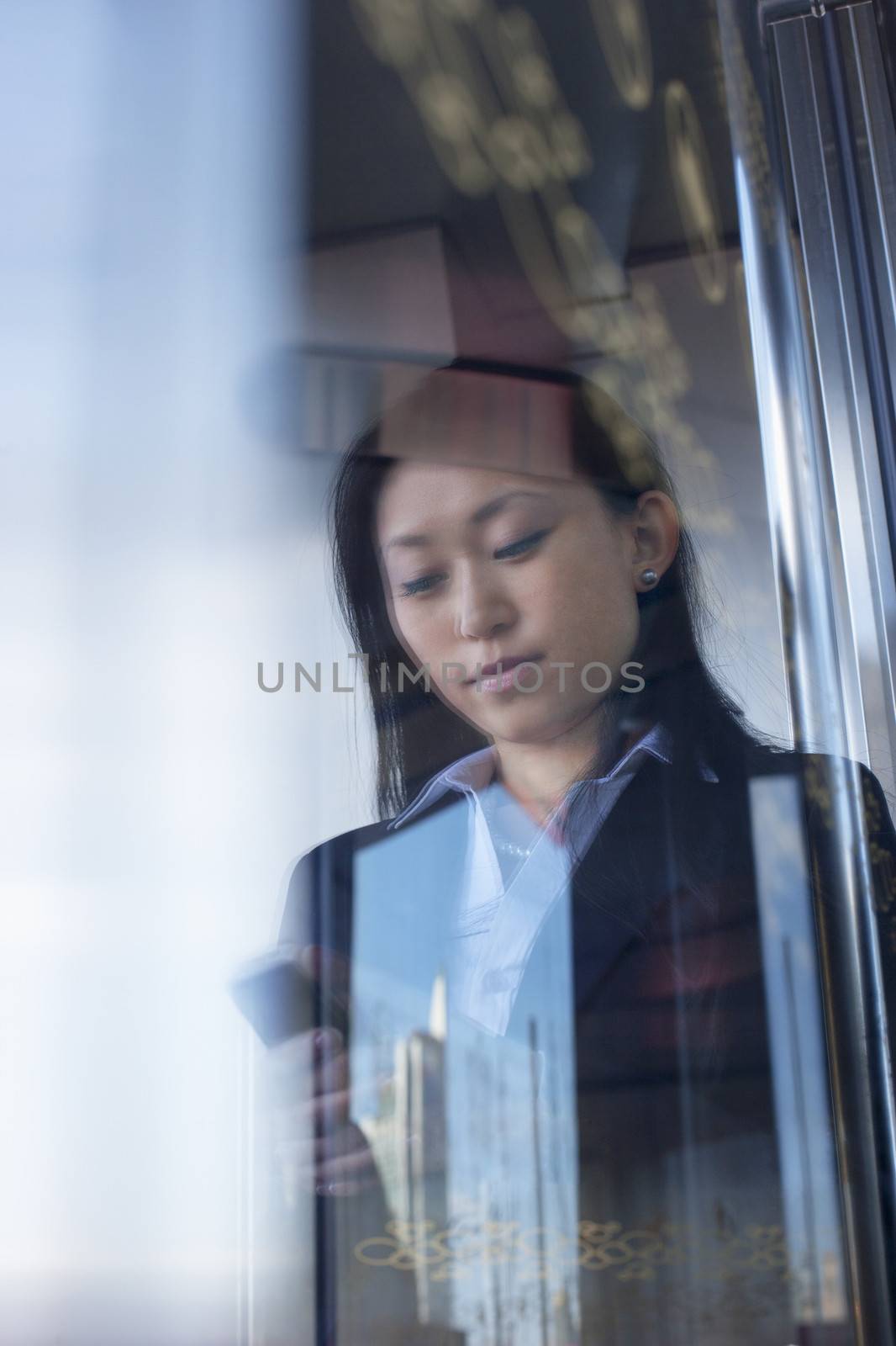 Young businesswoman looking down and using the phone on the other side the glass window