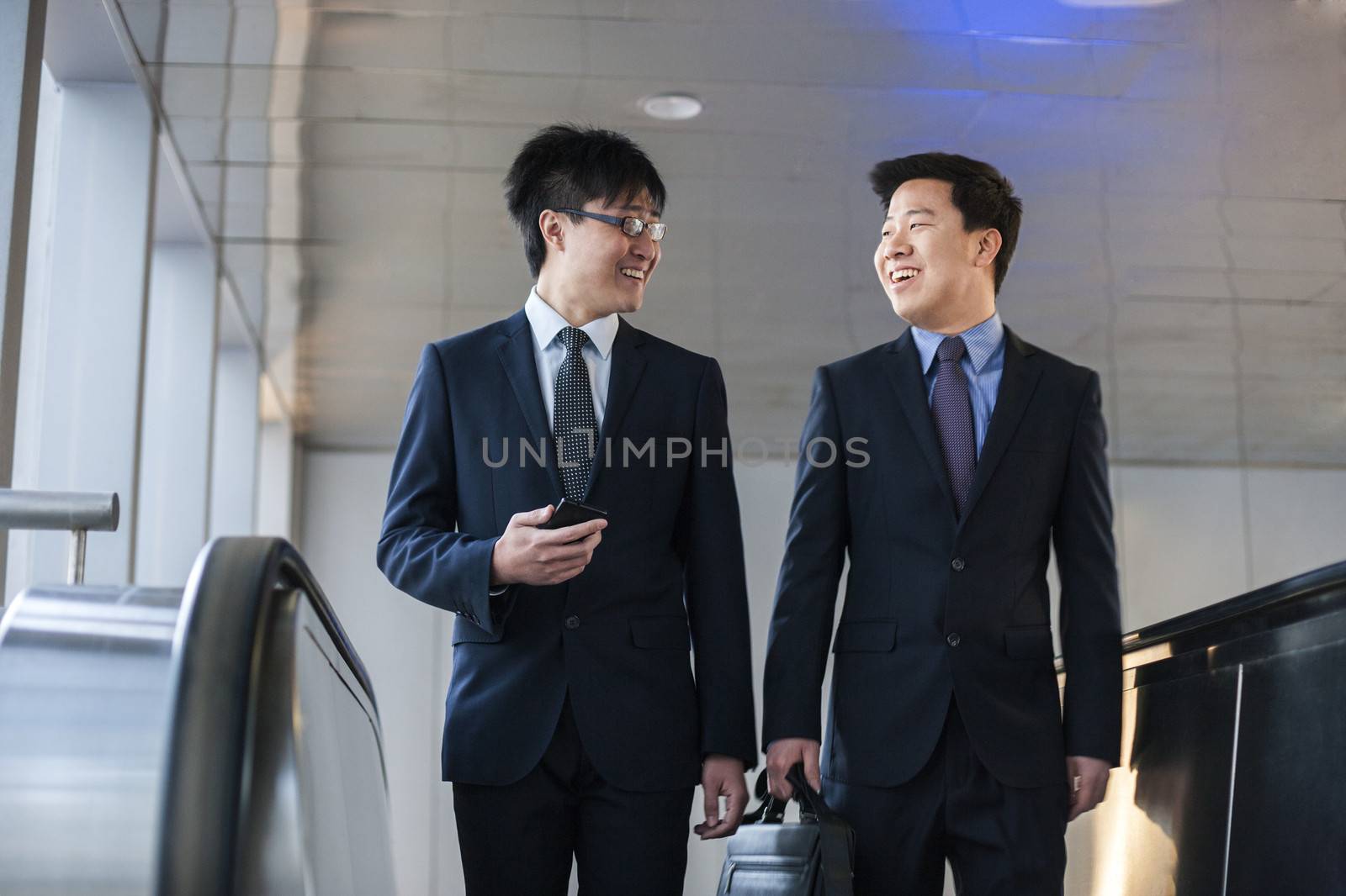 Two smiling businessmen coming up the escalator together by XiXinXing