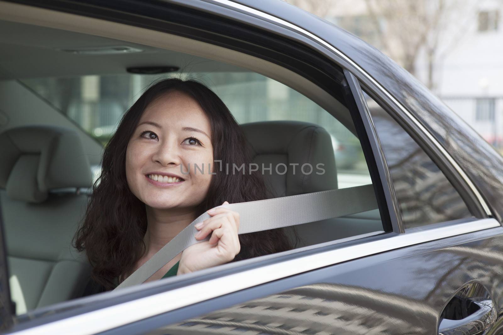 Young women in back seat of car fastening seat belt. by XiXinXing