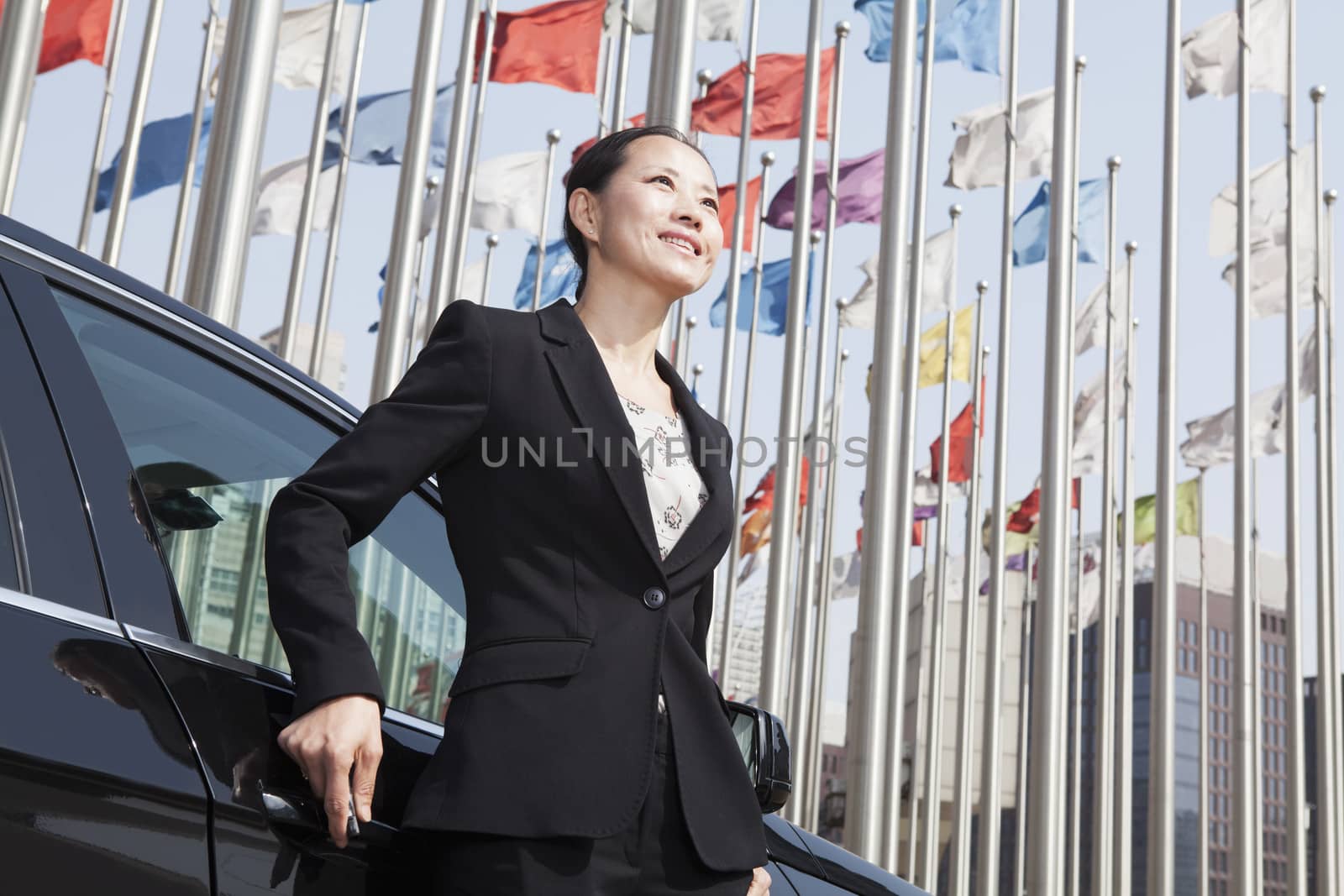 Businesswomen standing near car with flagpoles in background. by XiXinXing