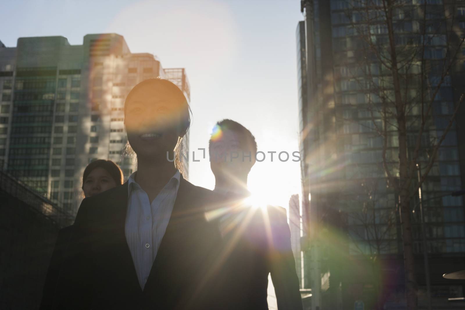 Three business people walking down a city street with sunlight at their back, lens flare by XiXinXing