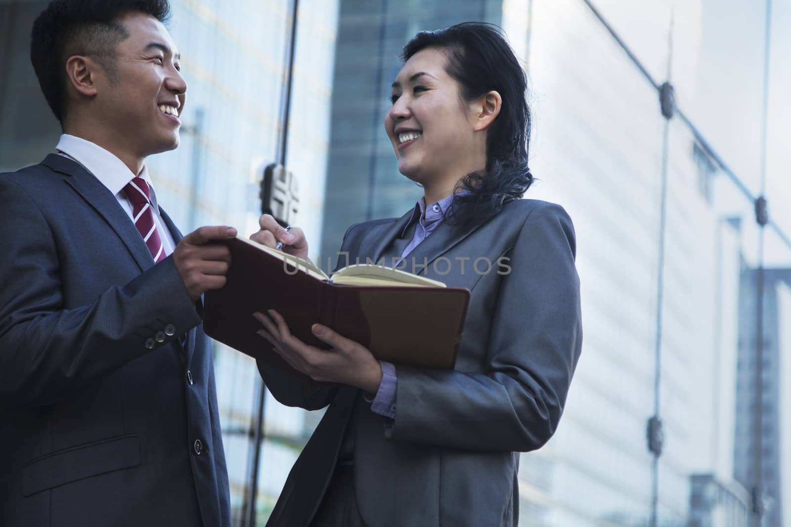 Two smiling business people outside meeting and writing in personal organizer by XiXinXing