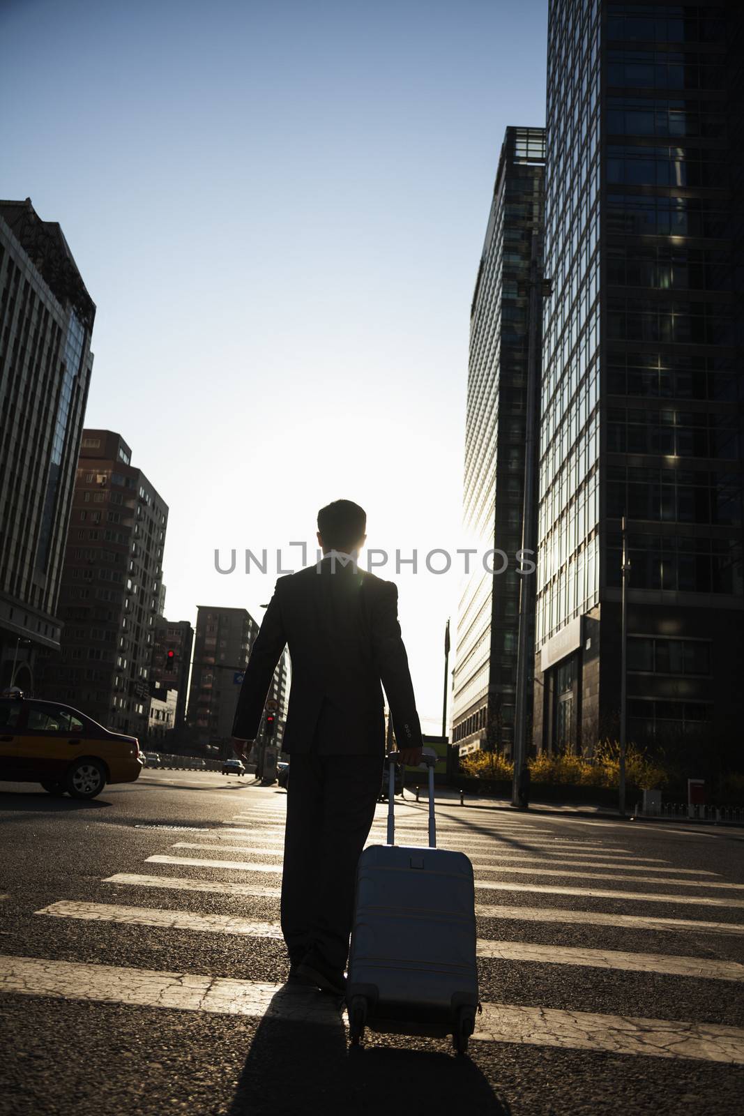 Rear view of young Businessman walking down the street with luggage