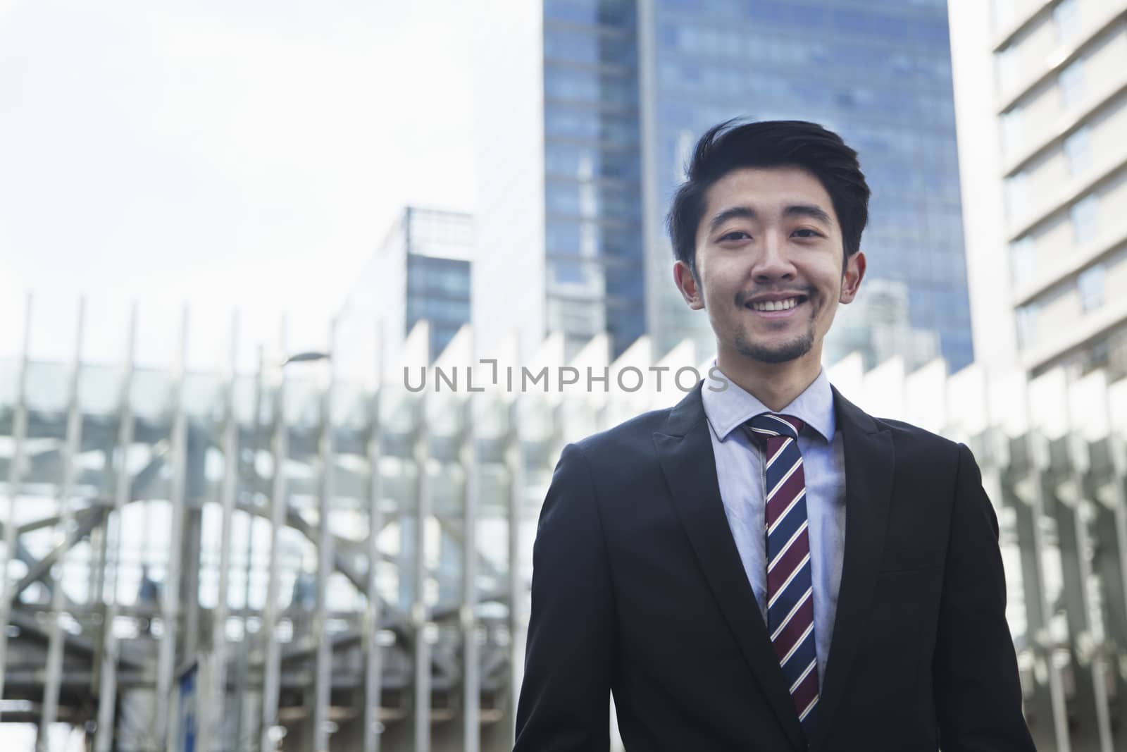 Portrait of smiling young businessman outdoors in Beijing, China by XiXinXing