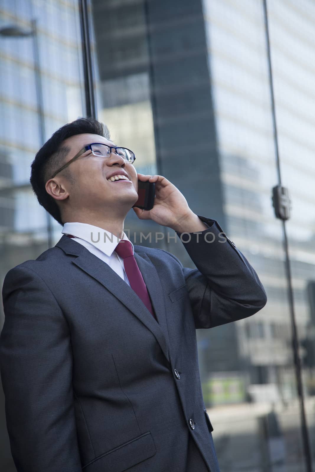 Smiling businessman on the phone outside in Beijing looking up by XiXinXing
