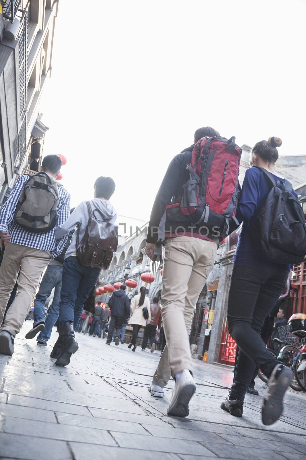 Group of young people walking down busy street, rear view.