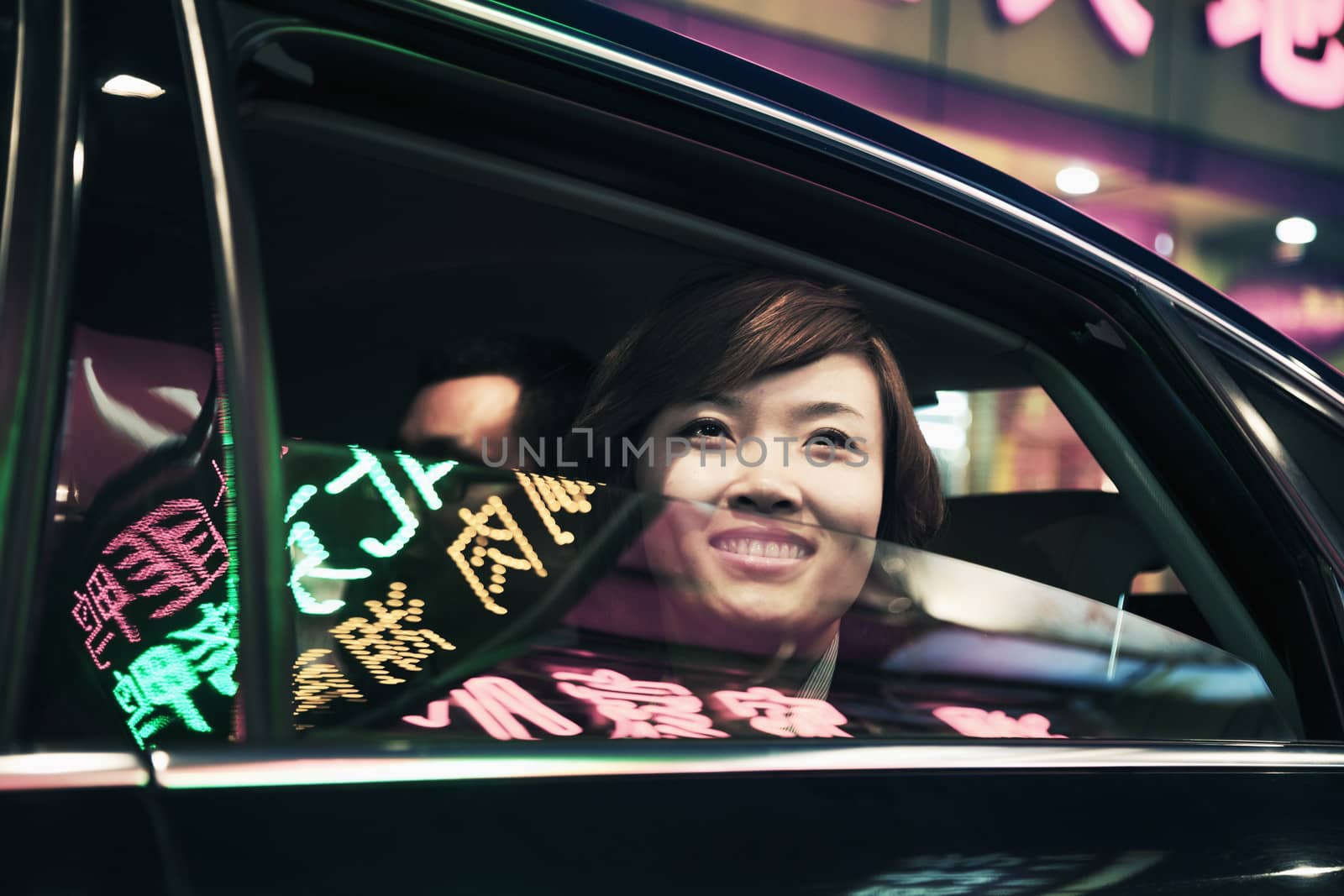 Smiling businesswoman with car window rolled down looking out at the nightlife in Beijing by XiXinXing