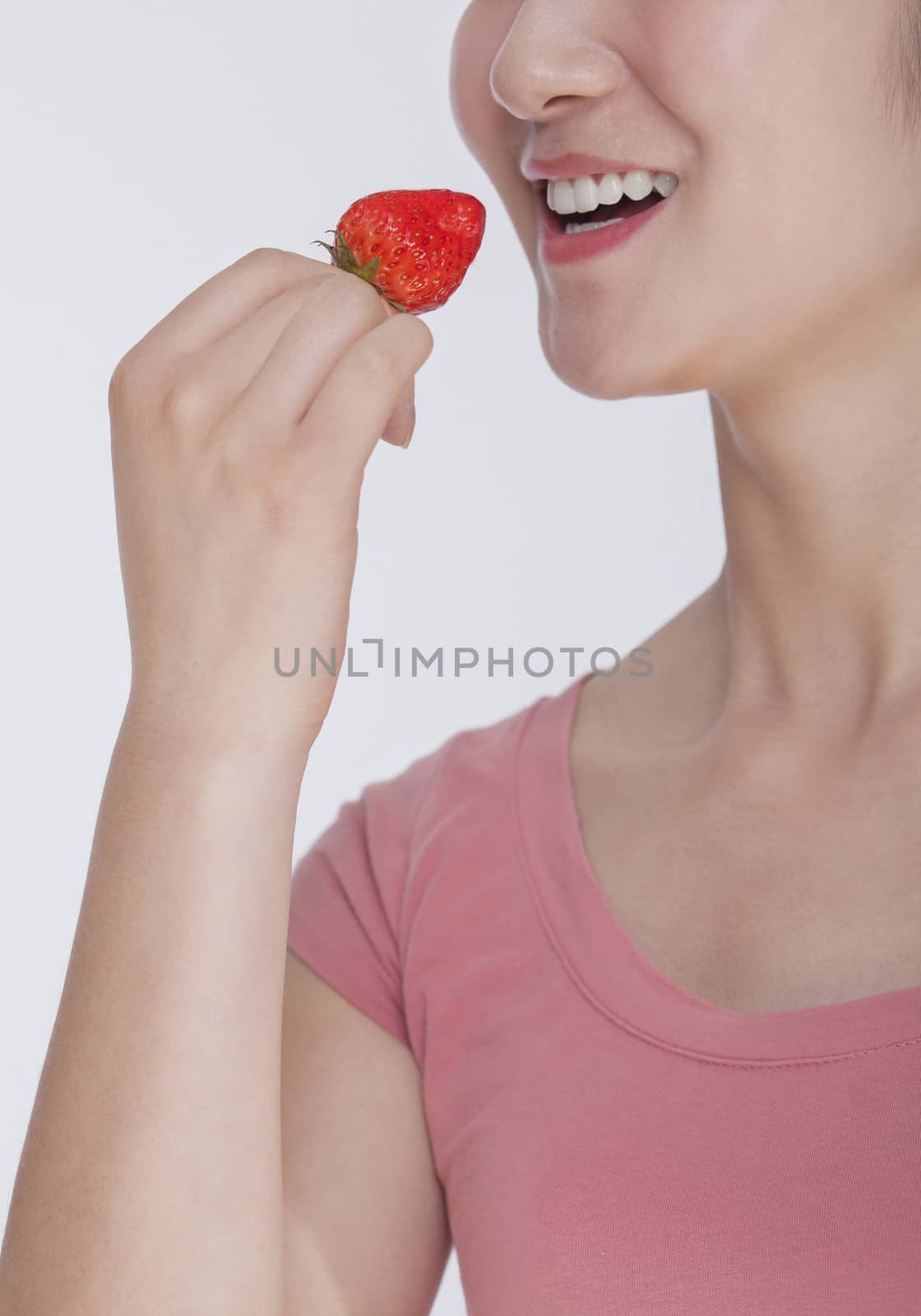 Young woman in pink shirt eating a strawberry, studio shot, half face showing