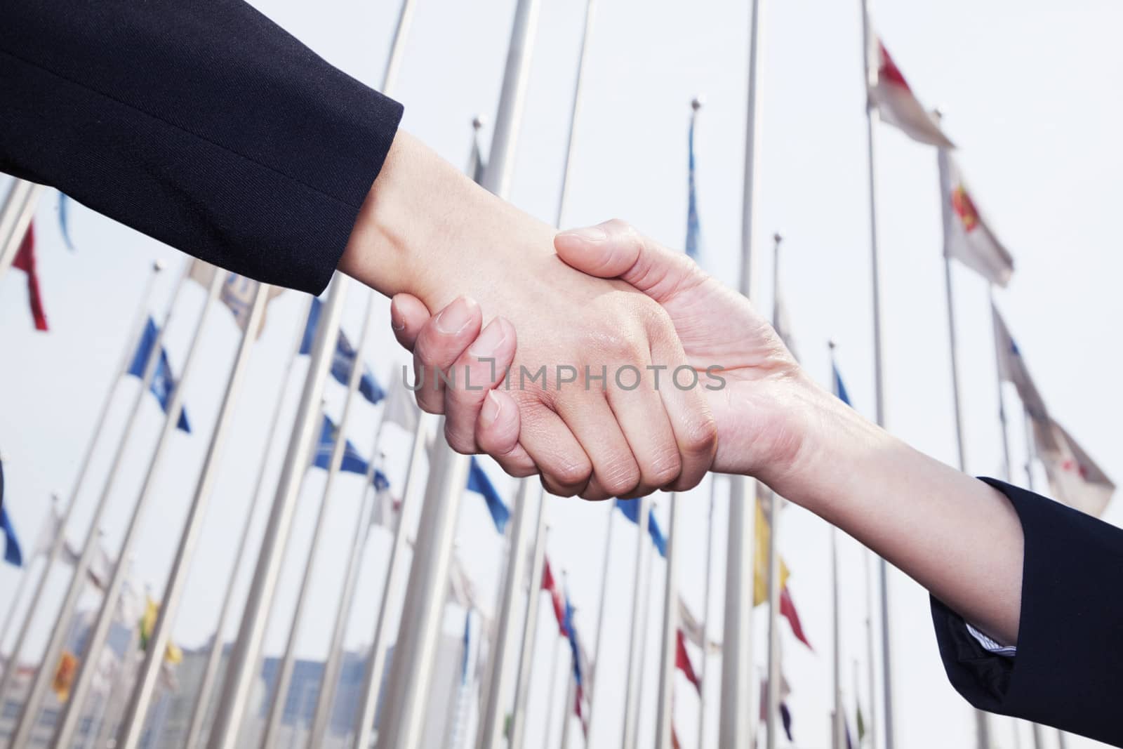 Two business people shaking hands in Beijing, flags flying in the background by XiXinXing