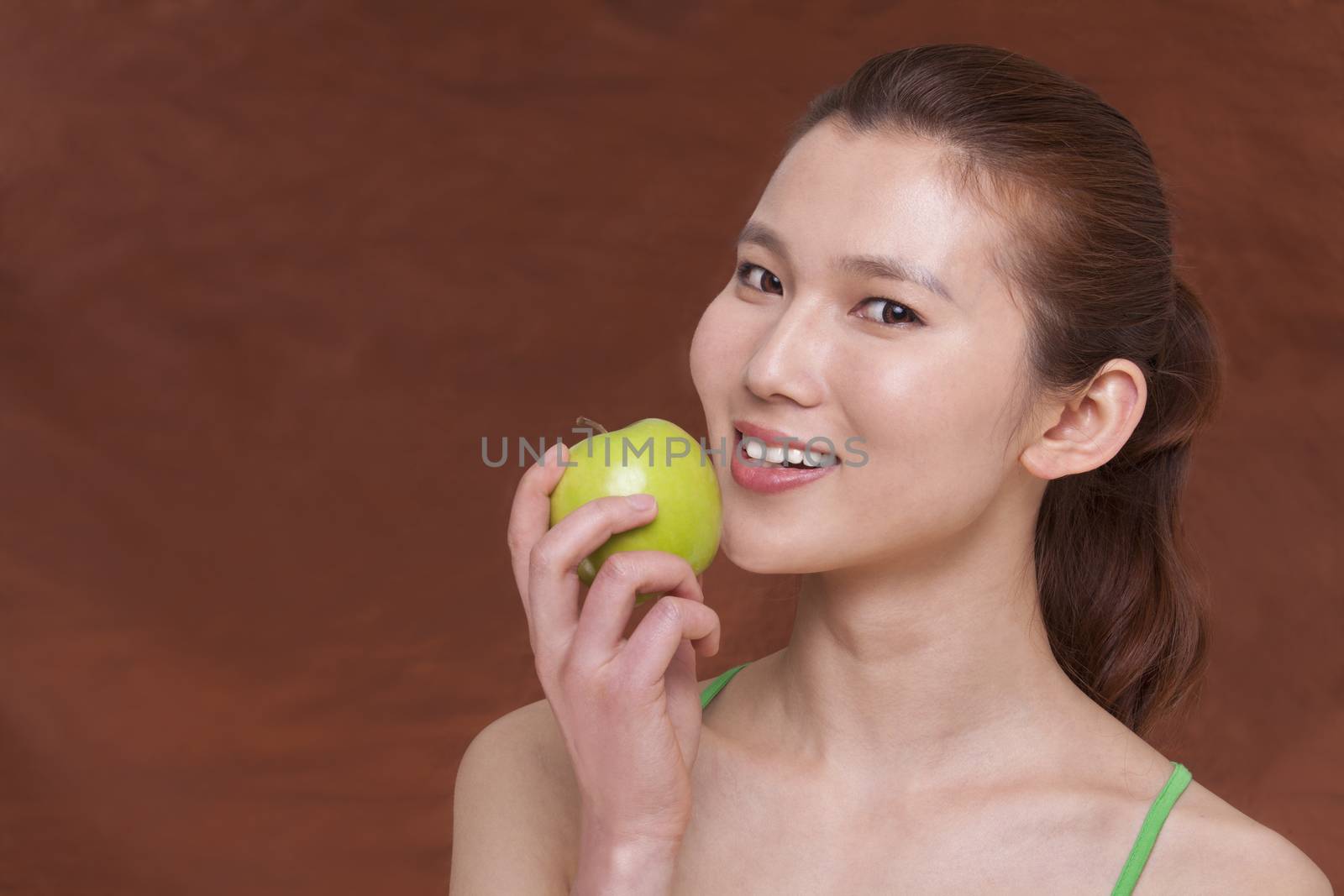 Young woman holding a apple and getting ready to take a bite, looking at camera, studio shot by XiXinXing