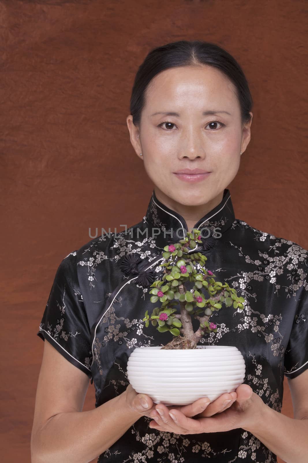 Portrait of woman in traditional clothing holding a small plant in a flower pot, studio shot