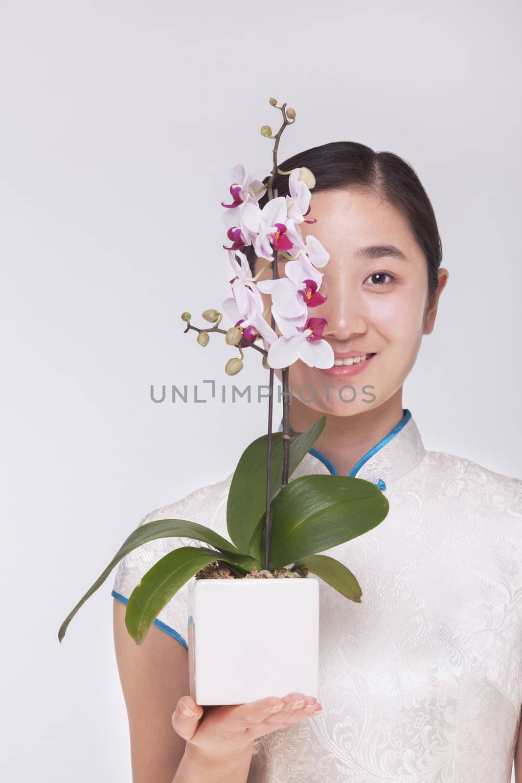 Portrait of smiling young woman holding a beautiful white flower in a flower pot, studio shot by XiXinXing