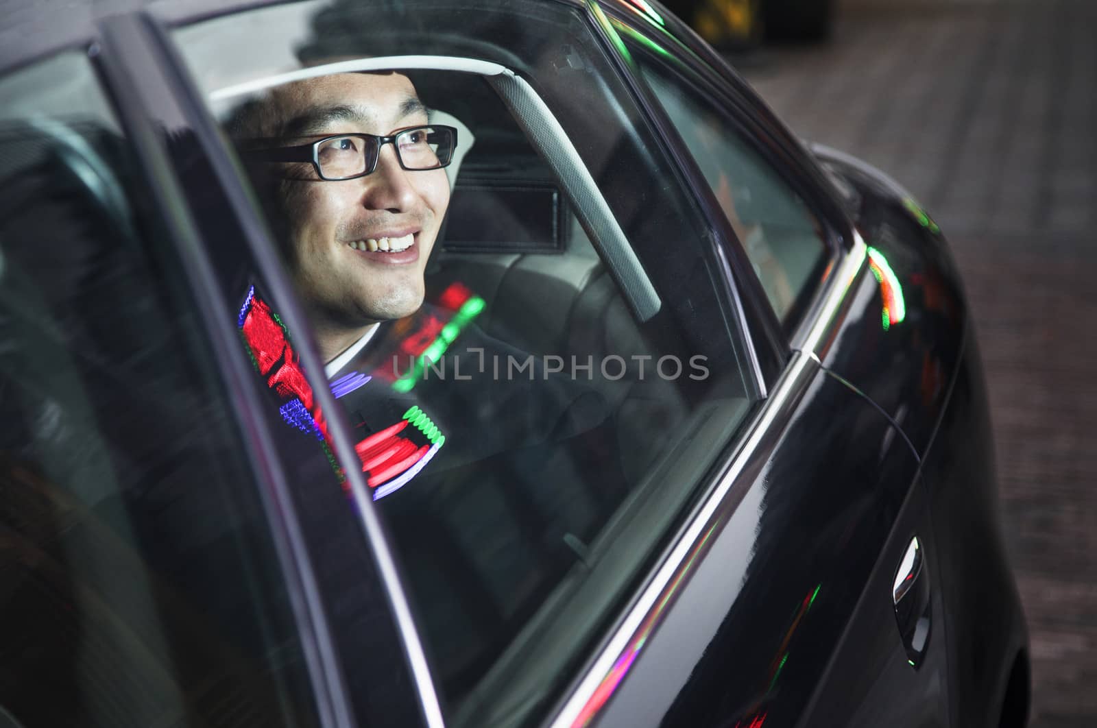 Smiling and happy businessman looking through car window at the night 