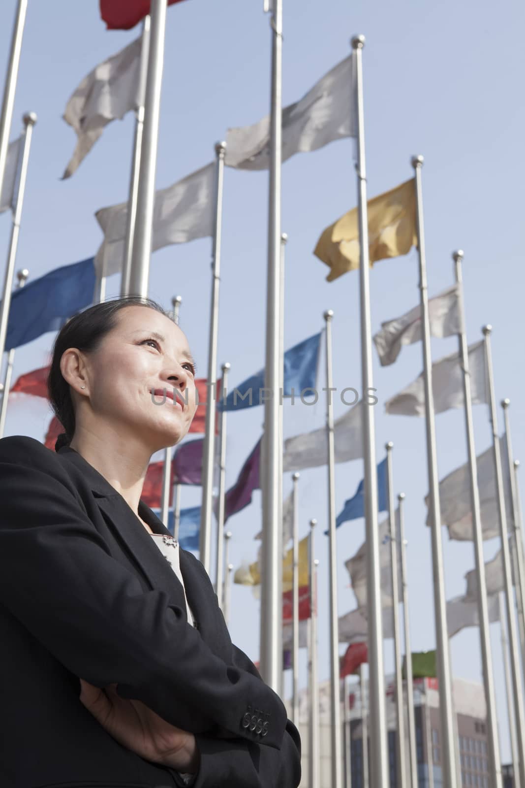 Businesswomen standing with arms crossed with flagpoles in background. by XiXinXing
