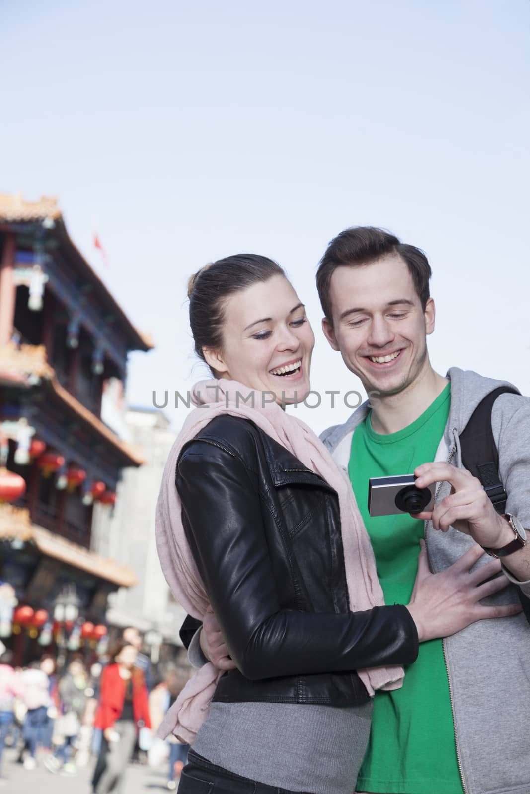 Young couple sightseeing, looking at digital camera. by XiXinXing
