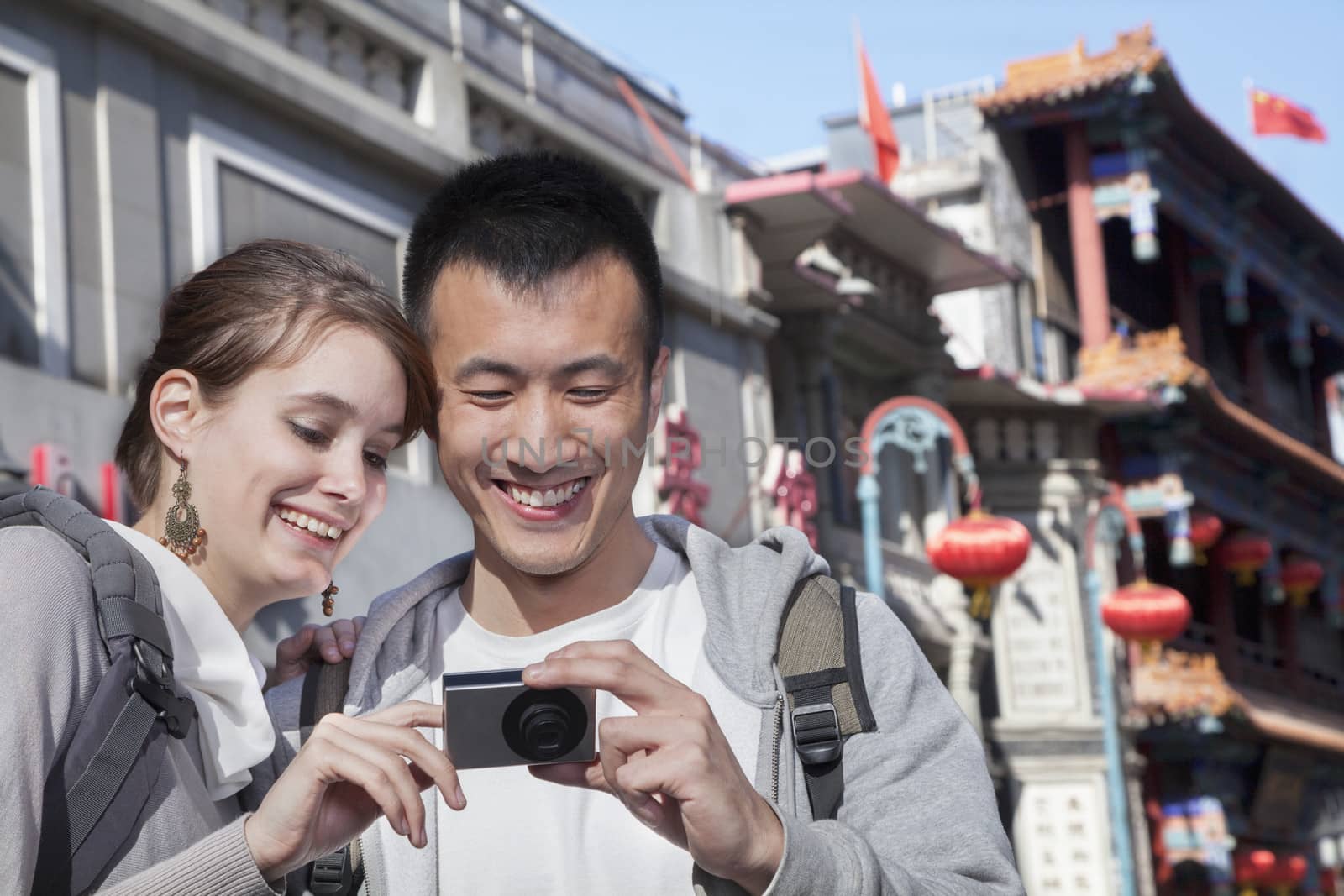 Young couple sightseeing, looking at digital camera. by XiXinXing