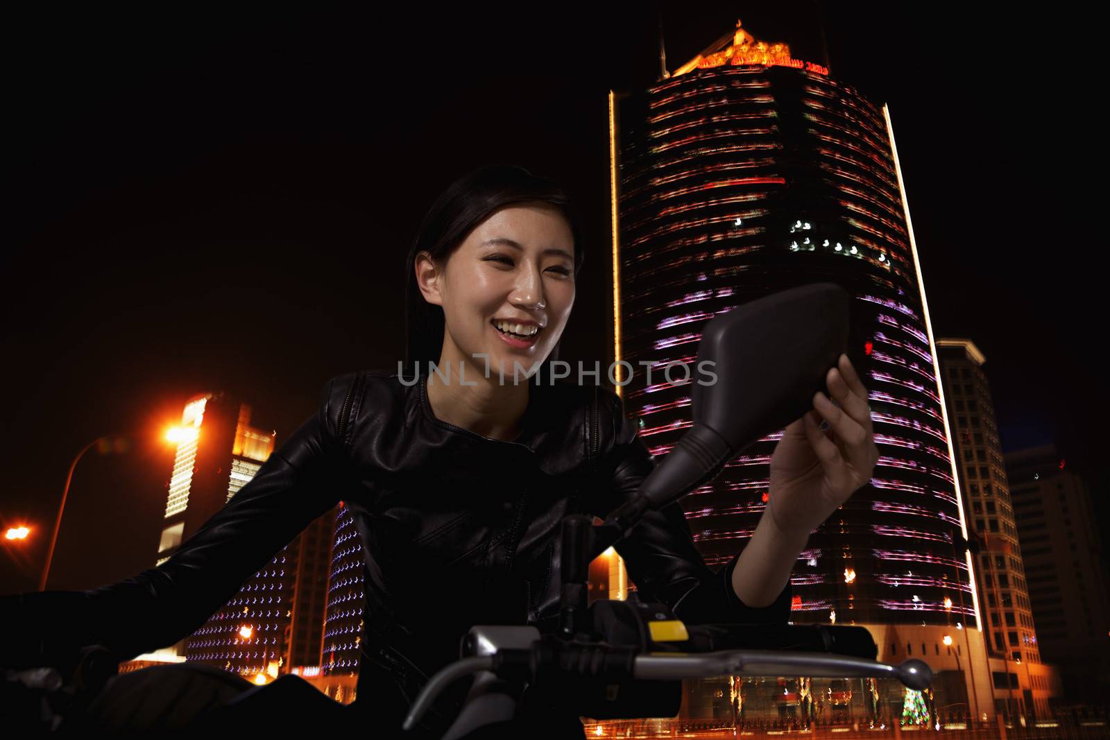 Beautiful young woman checking herself in the side mirror of a motorcycle, outdoors at night in Beijing