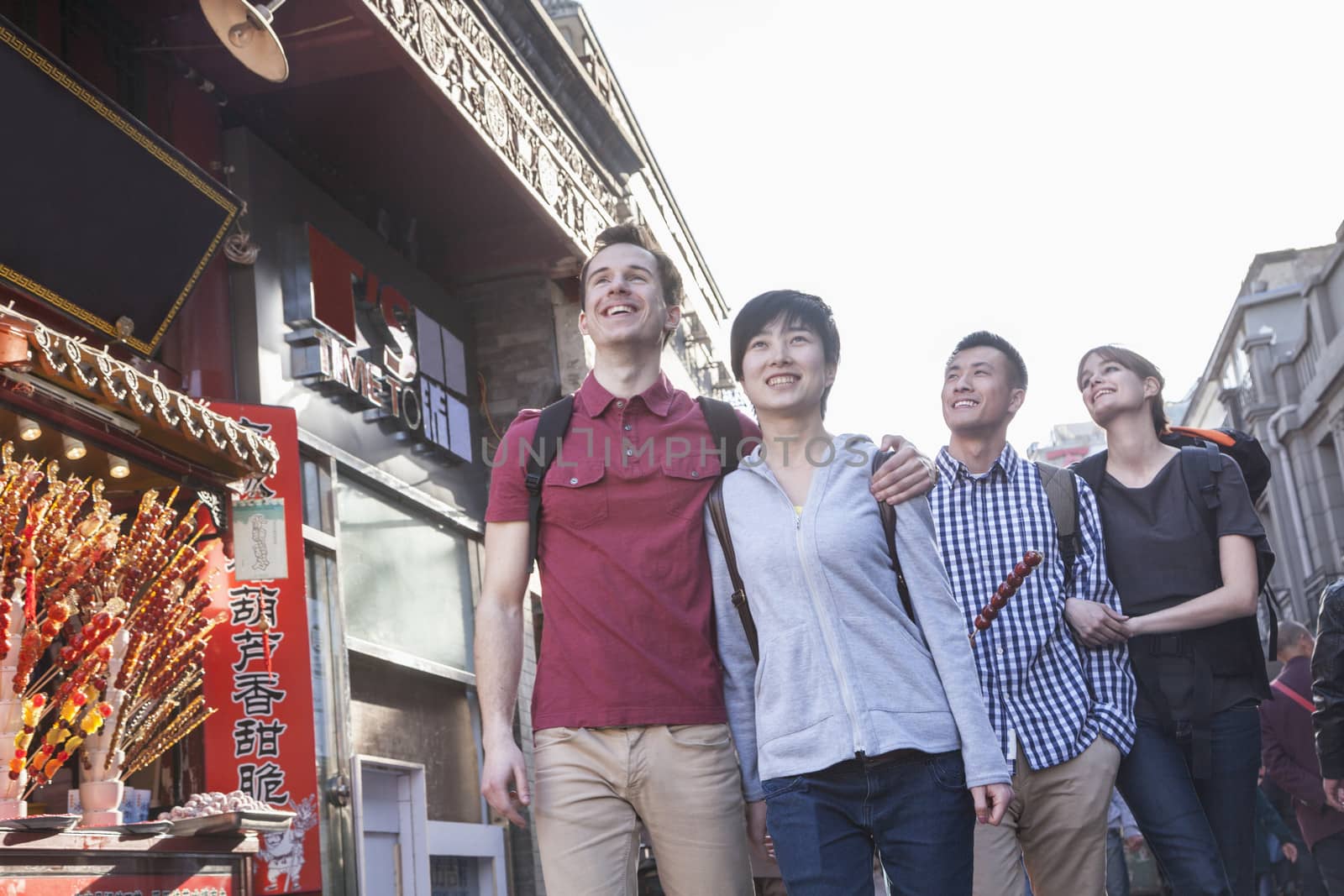 Four young people walking down street, near candied haw vendor.