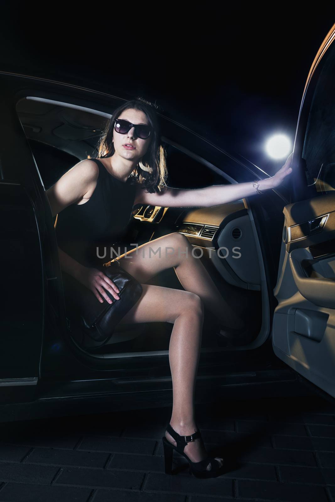 Young elegant woman stepping out of the car in sunglasses and evening dress at a red carpet event by XiXinXing