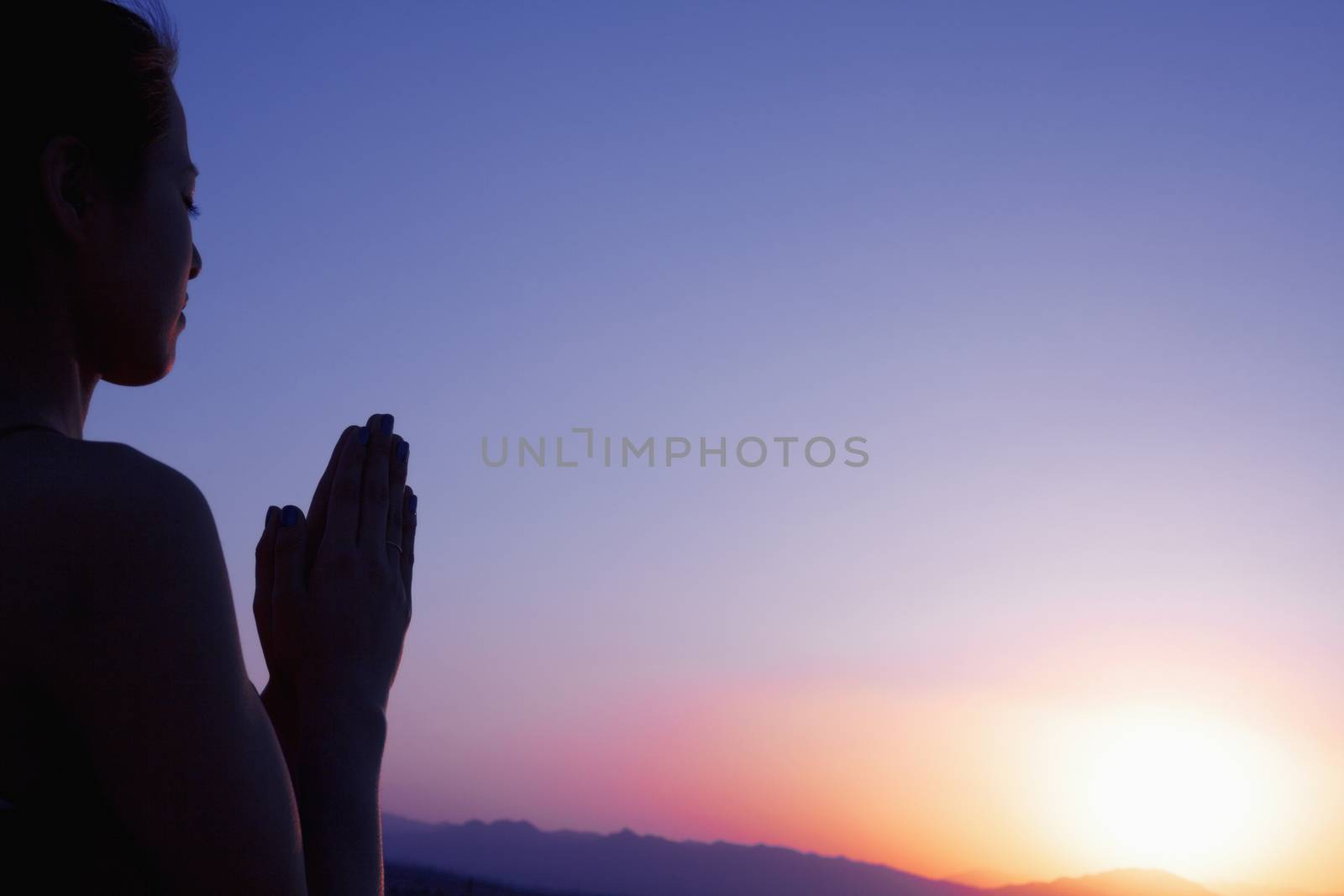 Serene young woman with hands together in prayer pose  in the desert in China, silhouette, sun setting by XiXinXing