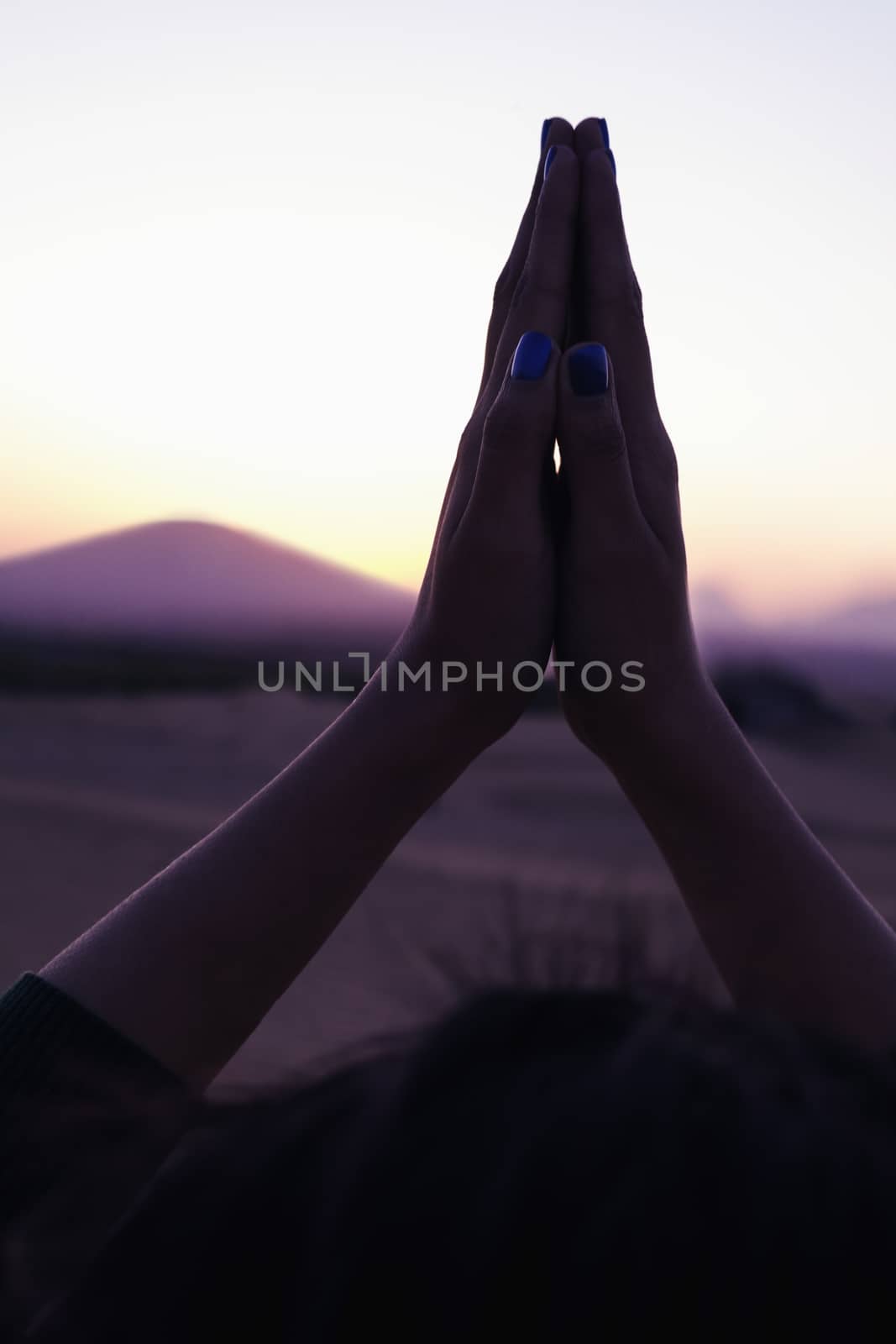 Serene young woman with her palms together in prayer held above her head in the desert in China, close-up