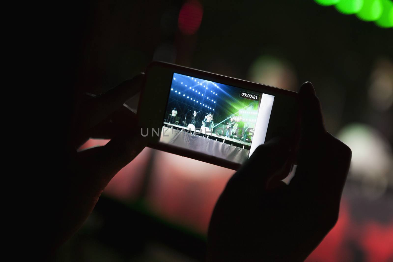 Young woman taking a photography with her smart phone at an indoor concert, Close-up on hands by XiXinXing