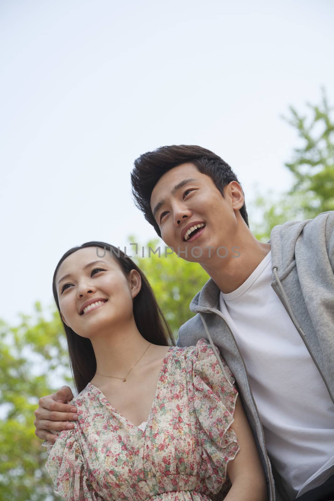 Smiling happy young couple with arm around the shoulders outdoors in a park, front view by XiXinXing
