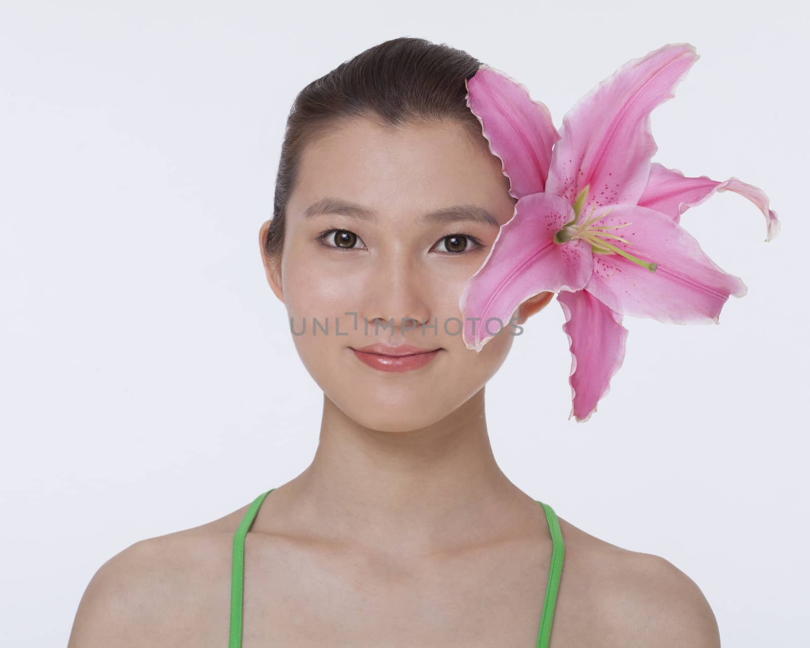 Portrait of young, smiling, beautiful woman with a large pink flower tucked behind her ear, studio shot by XiXinXing