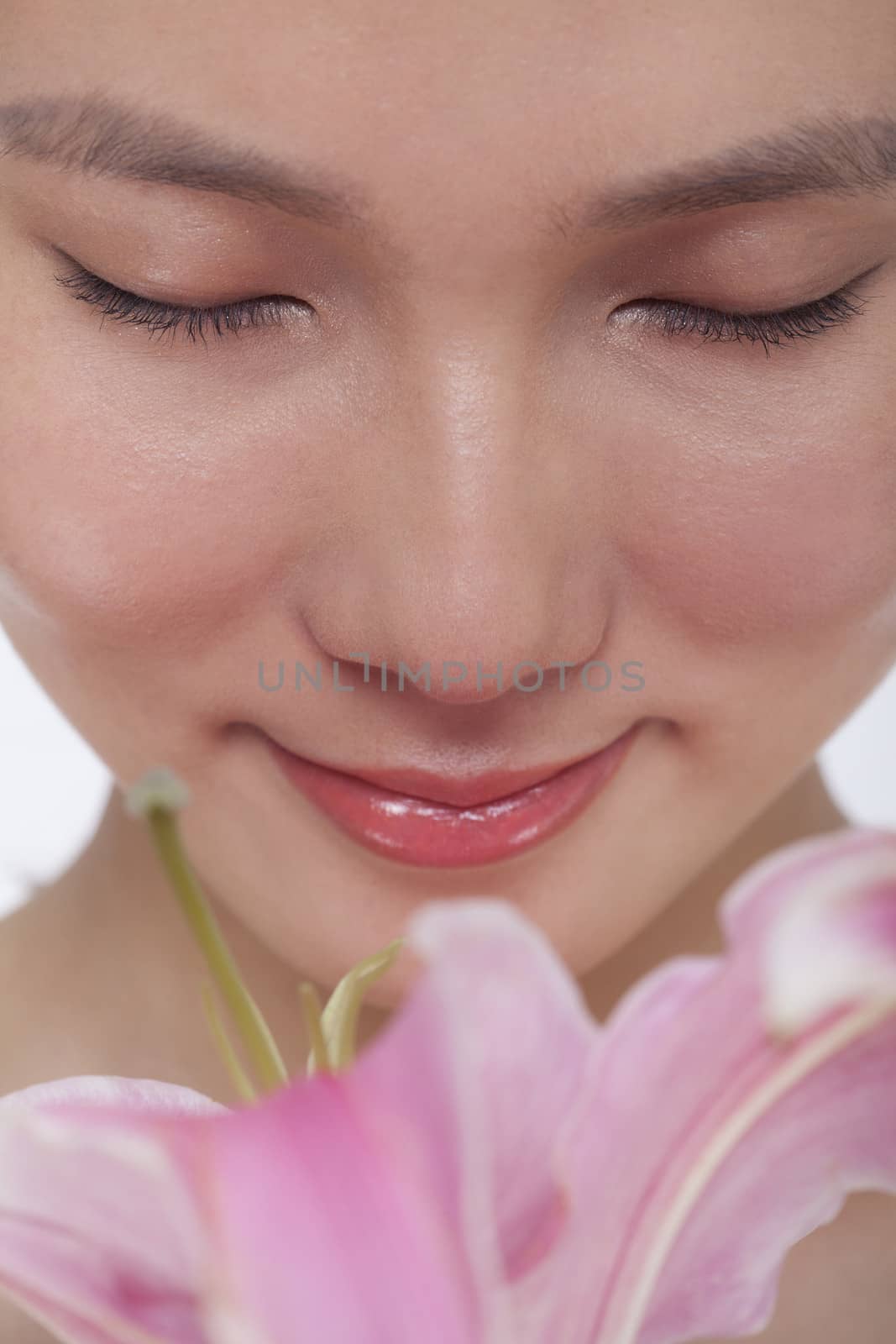 Close -Up of young beautiful woman smelling a  large pink flower, studio shot