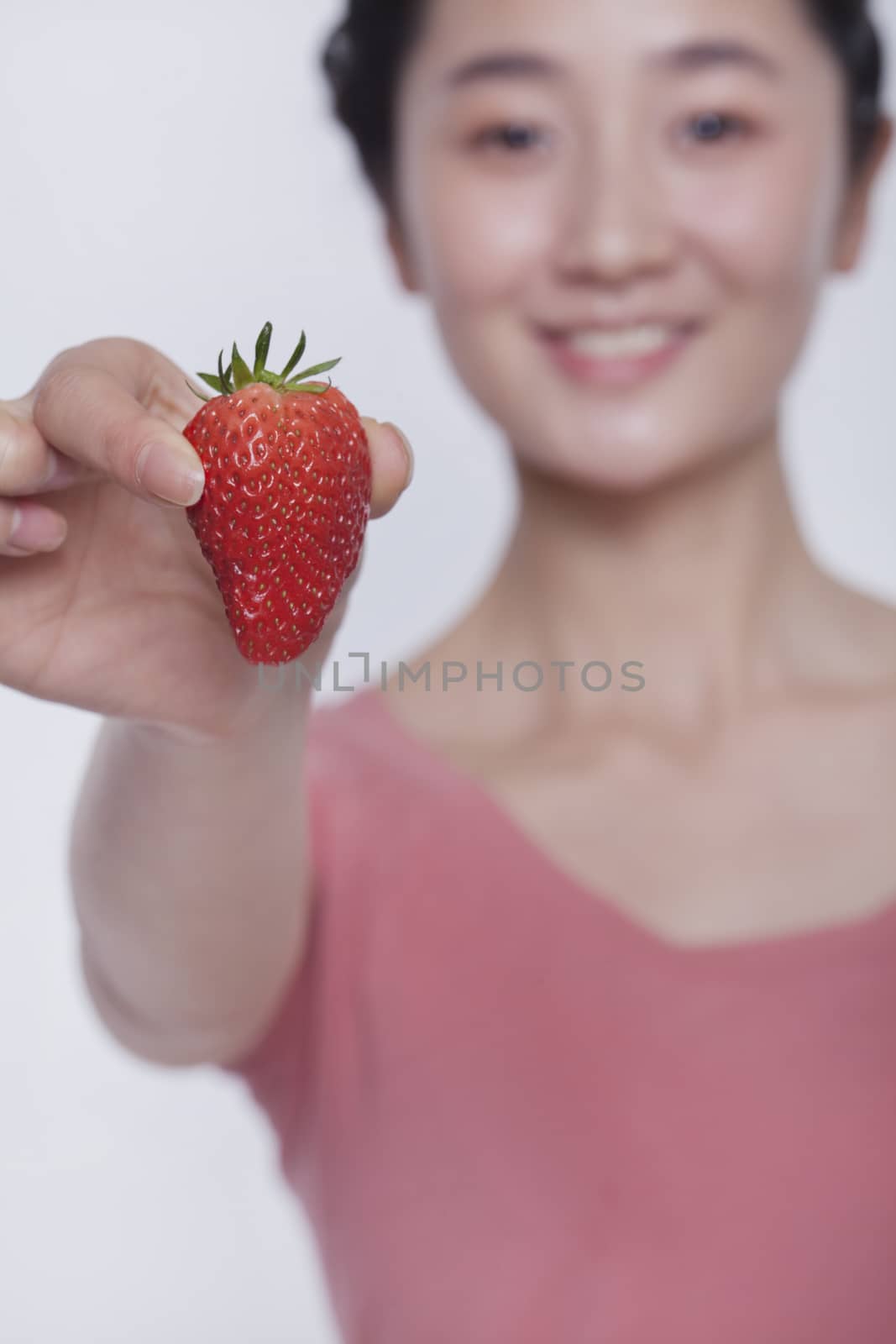 Young smiling woman in pink shirt holding and showing a strawberry  by XiXinXing