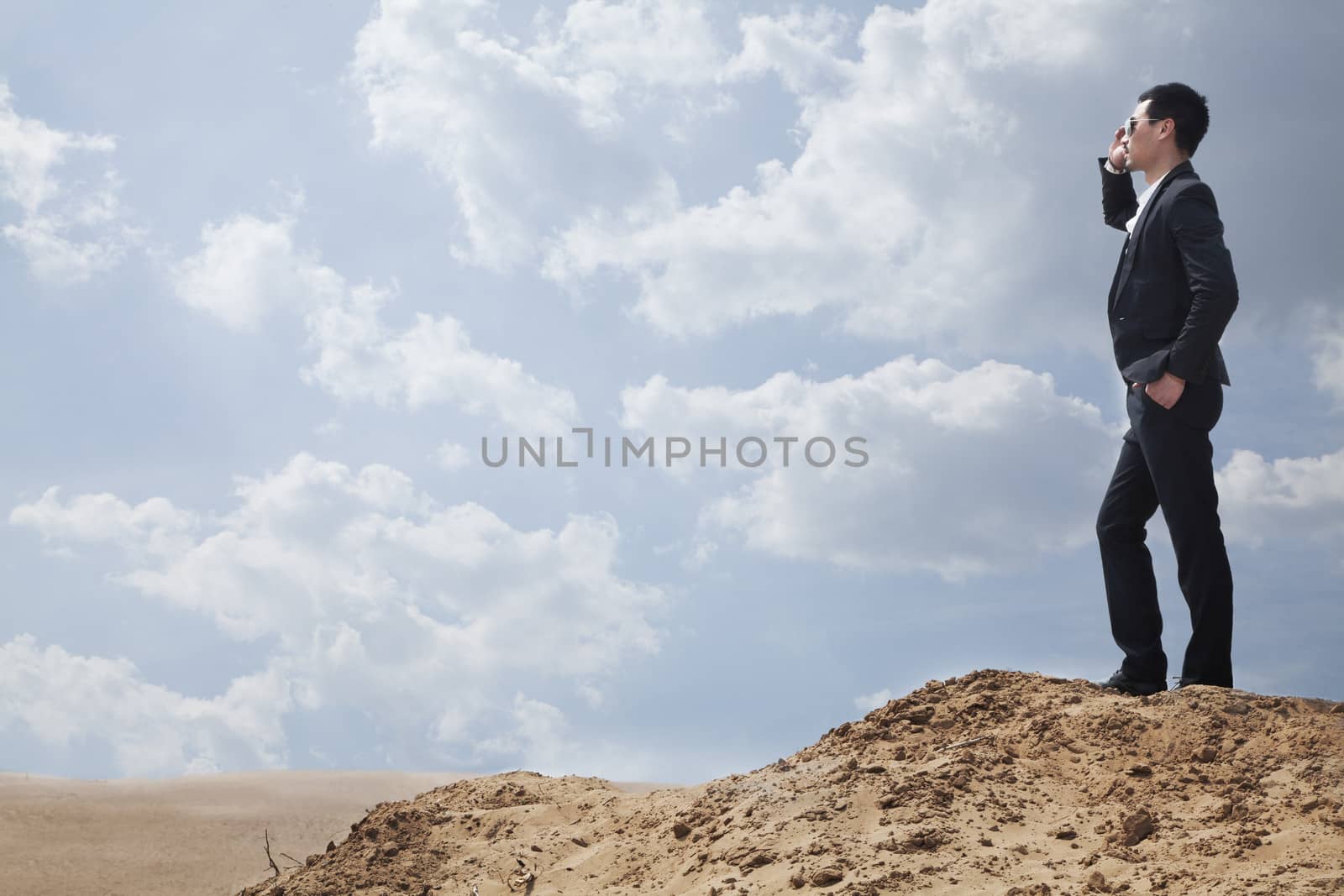 Young businessman in sunglasses standing in the desert and talking on the phone