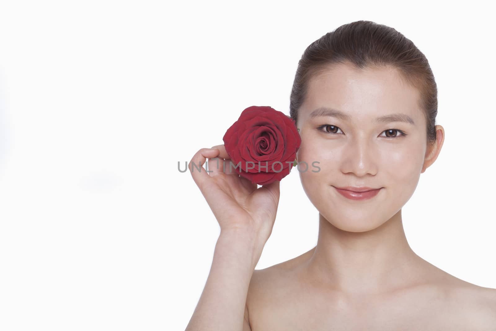Smiling young woman holding up a red rose next to her ear, studio shot by XiXinXing