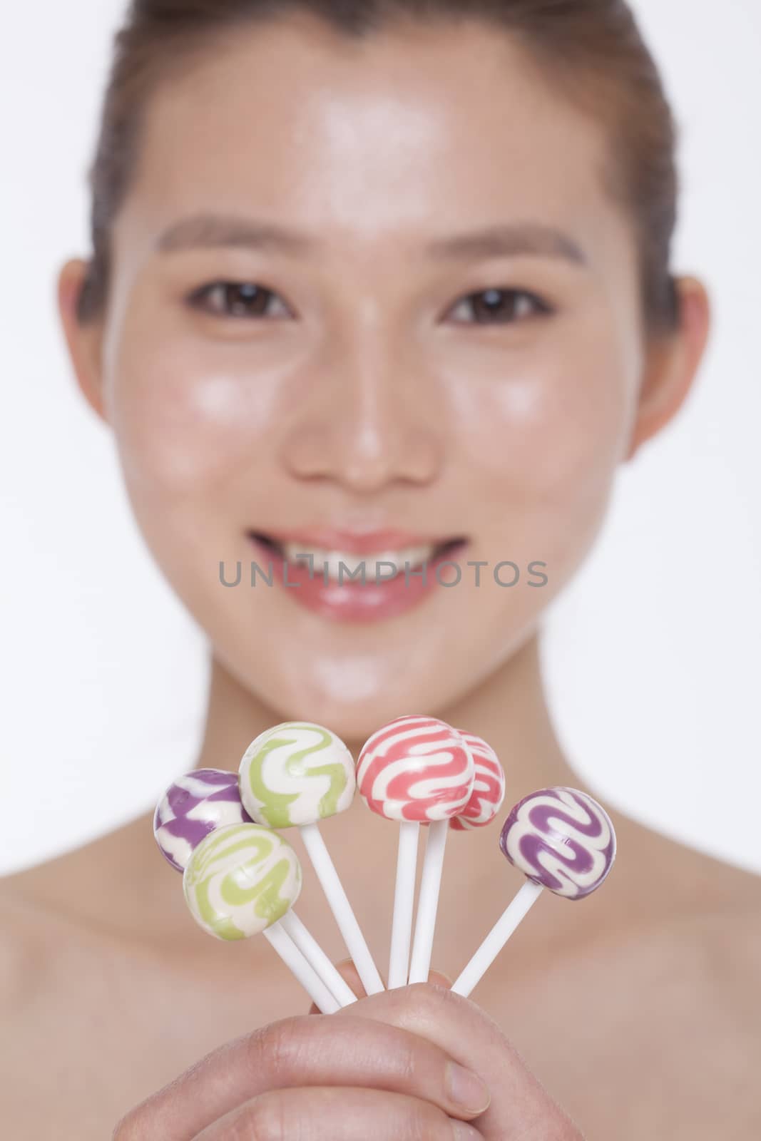 Smiling young woman looking into camera and holding up colorful lollipops, studio shot by XiXinXing