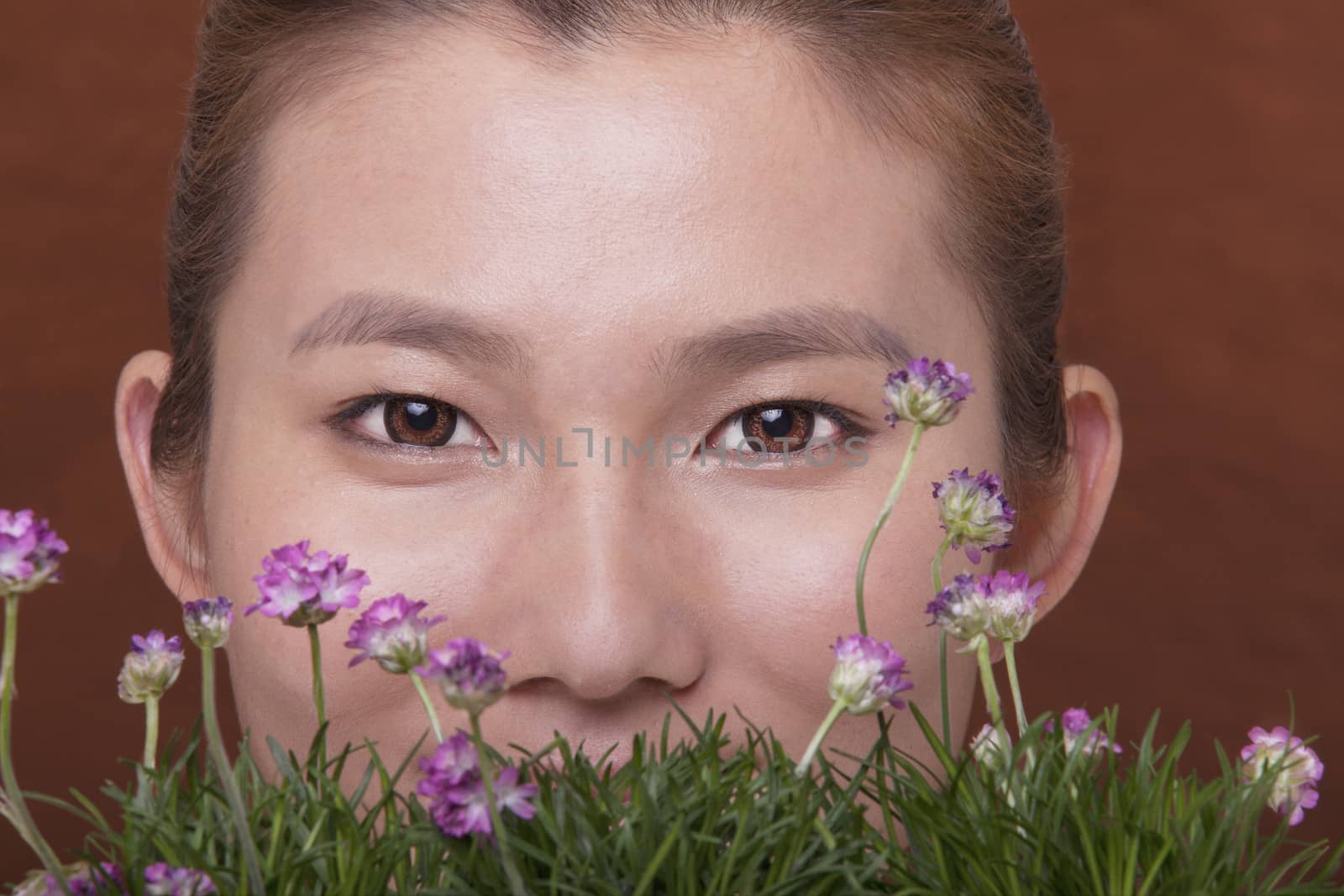 Close- up portrait of young woman with her face behind some flowers and grass, studio shot