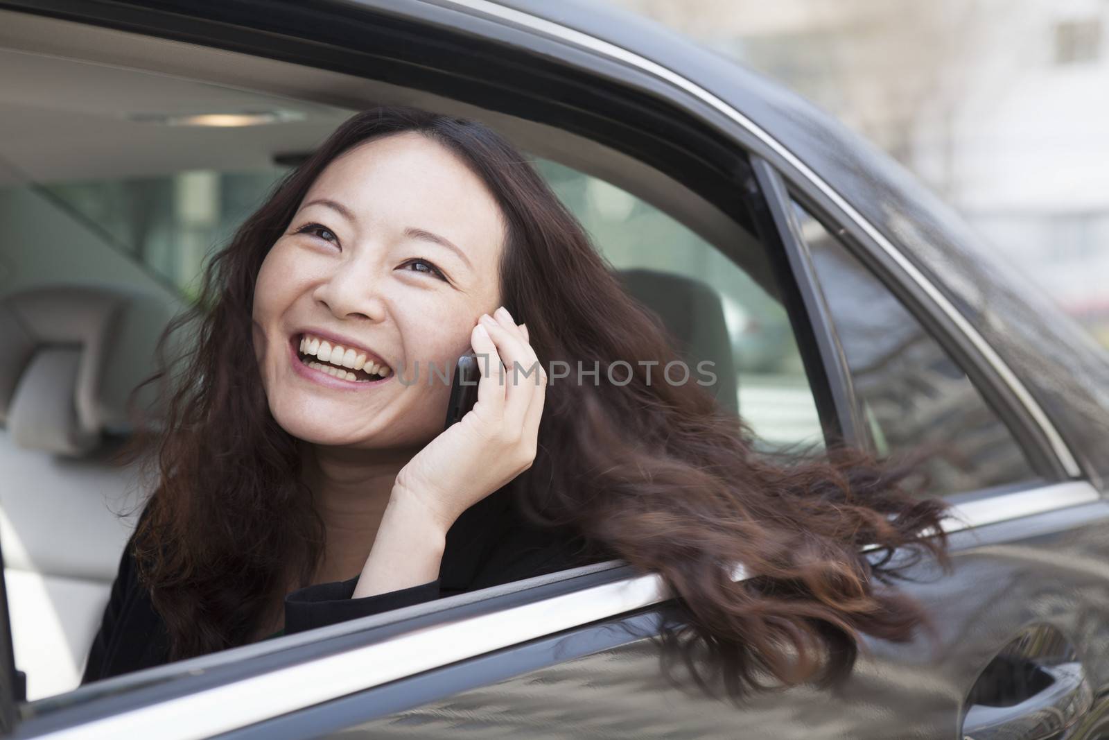 Young women in back seat of car using mobile phone. by XiXinXing