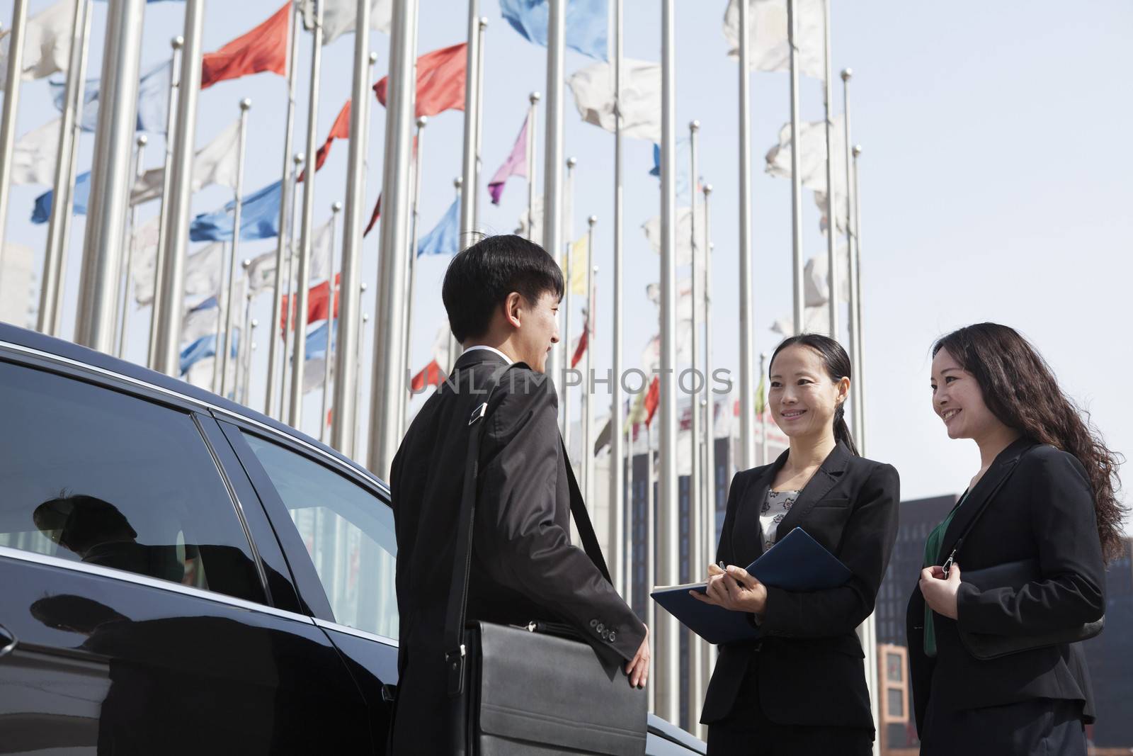 Three businesspeople meeting outdoors with flagpoles in background. by XiXinXing