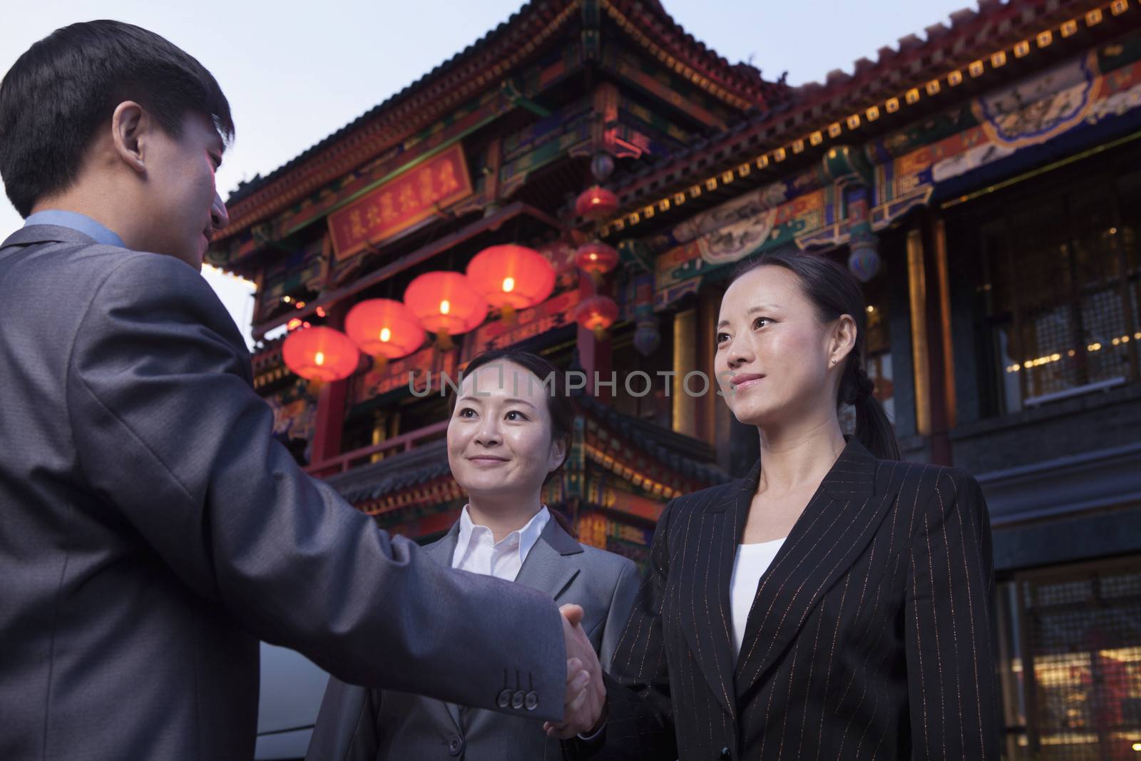 Three businesspeople meeting outdoors with Chinese architecture in background.