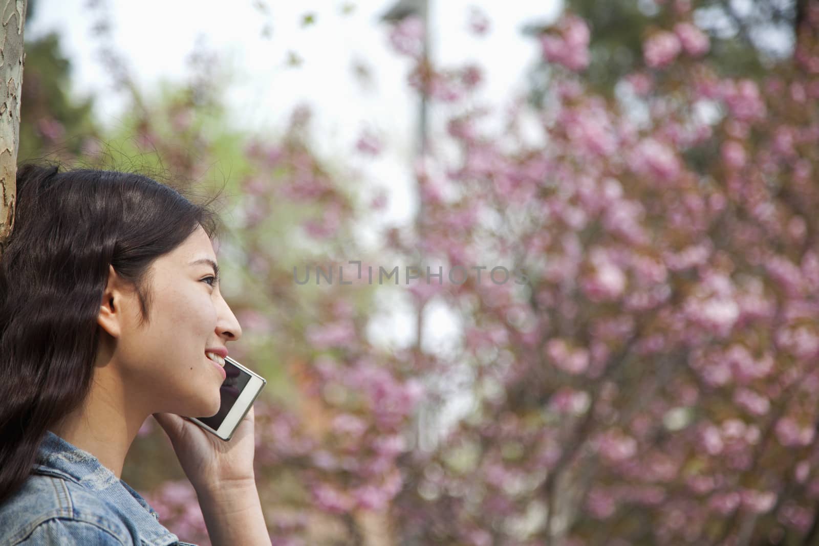 Side view of young woman talking on the phone outdoors in the park in springtime