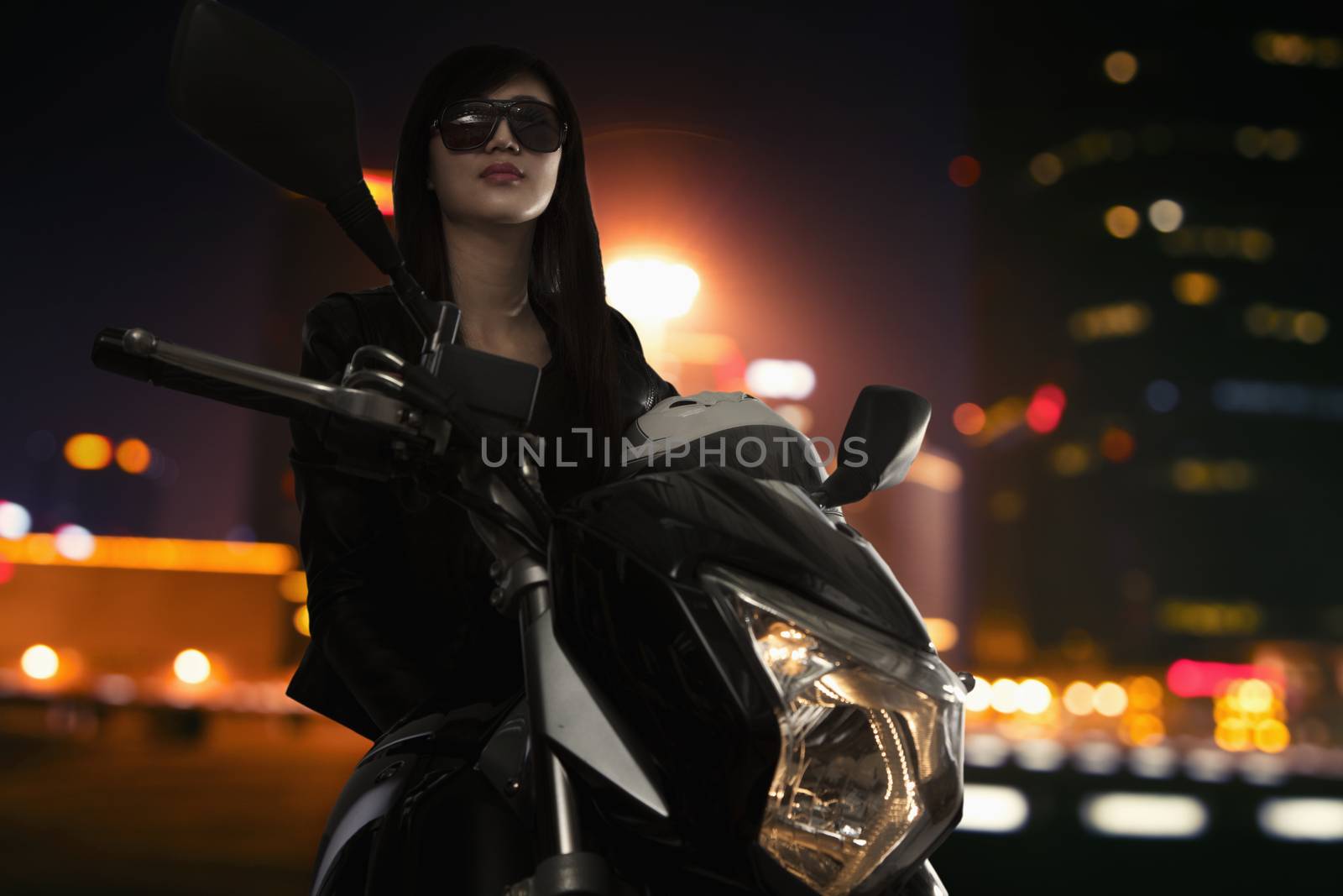 Beautiful young woman in sunglasses sitting on a motorcycle at night time in Beijing
