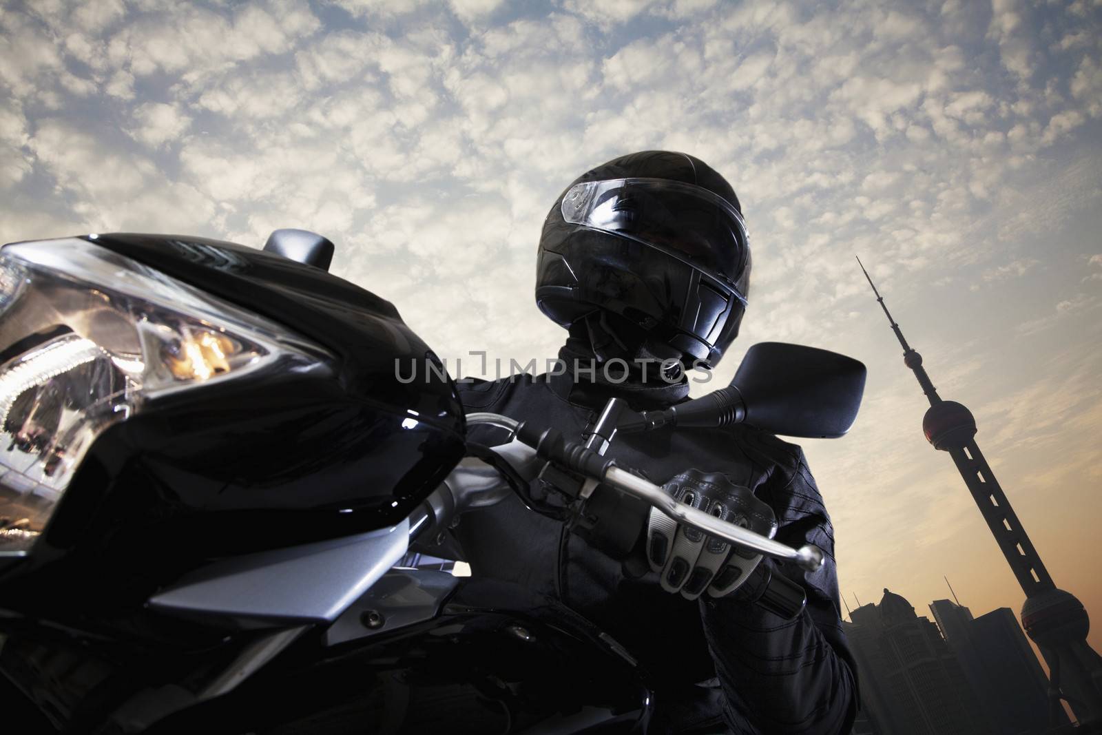 Young man riding a motorcycle during the day, sky and building exteriors in the background