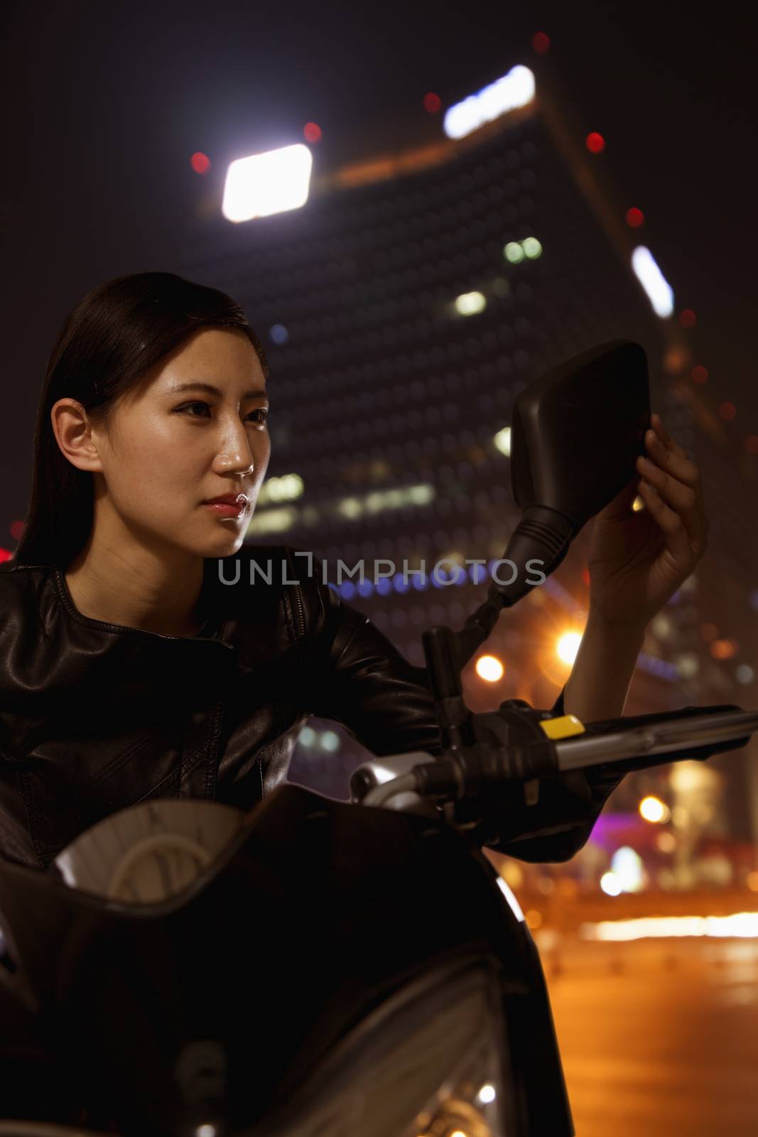 Beautiful young woman checking herself in the side mirror of a motorcycle, outdoors at night in Beijing