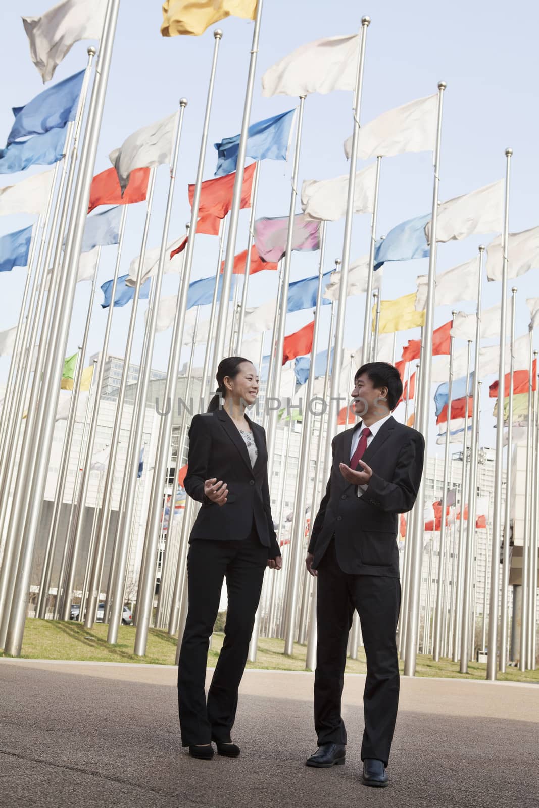 Two businesspeople meeting outdoors with flagpoles in background.