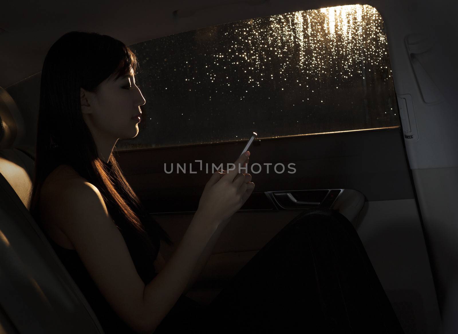 Young woman sitting in the car and texting on her phone on a rainy night in Beijing