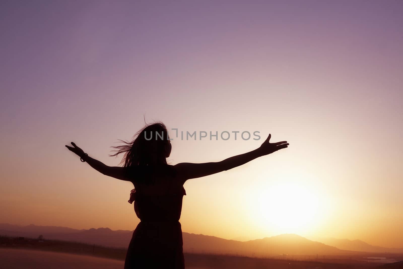Serene young woman with arms outstretched doing yoga in the desert in China, Silhouette by XiXinXing