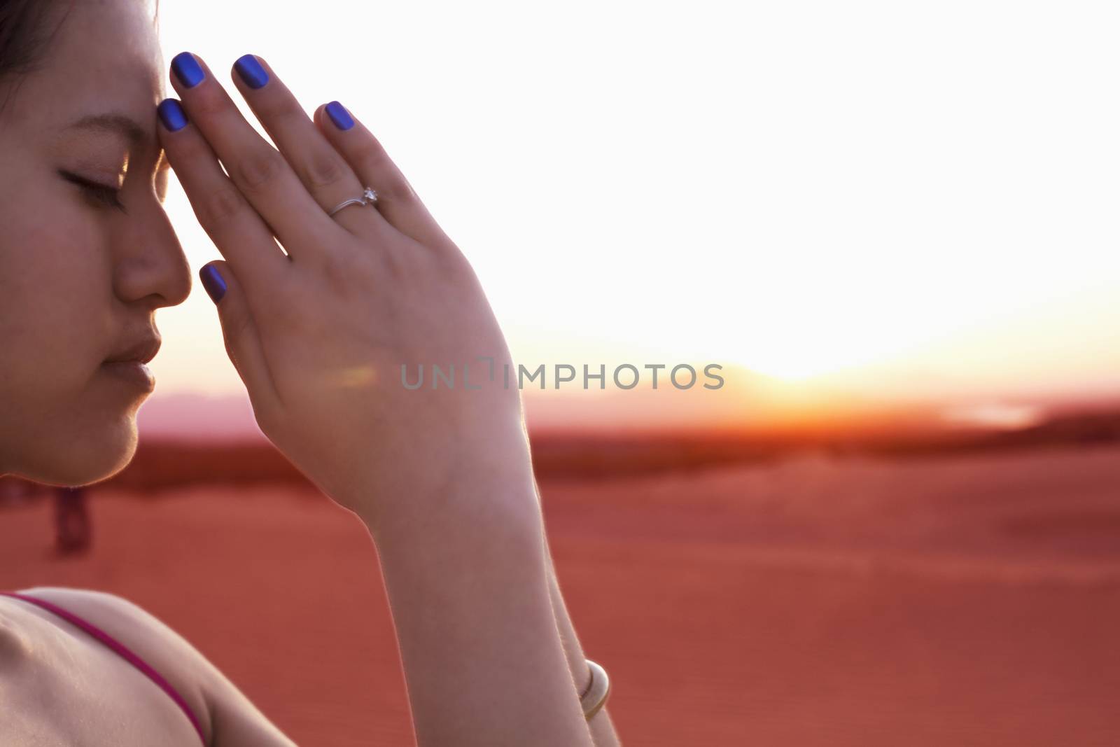 Serene young woman with eyes closed and hands together in prayer pose in the desert in China, side view