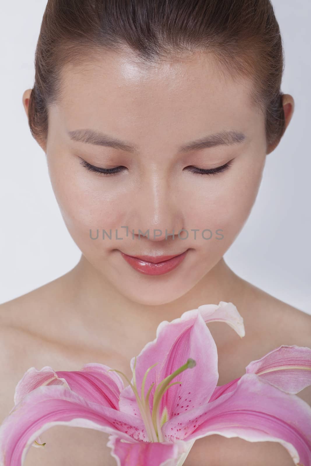 Young tranquil woman looking down at a large pink flower, studio shot by XiXinXing