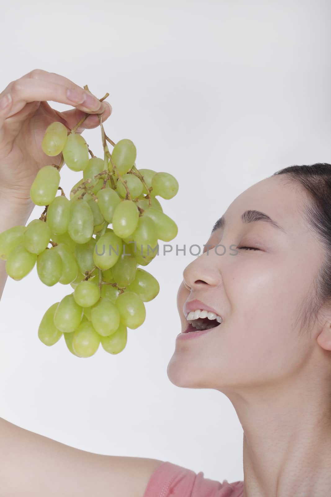 Young woman enjoying a bunch of grapes raised above her head, studio shot by XiXinXing
