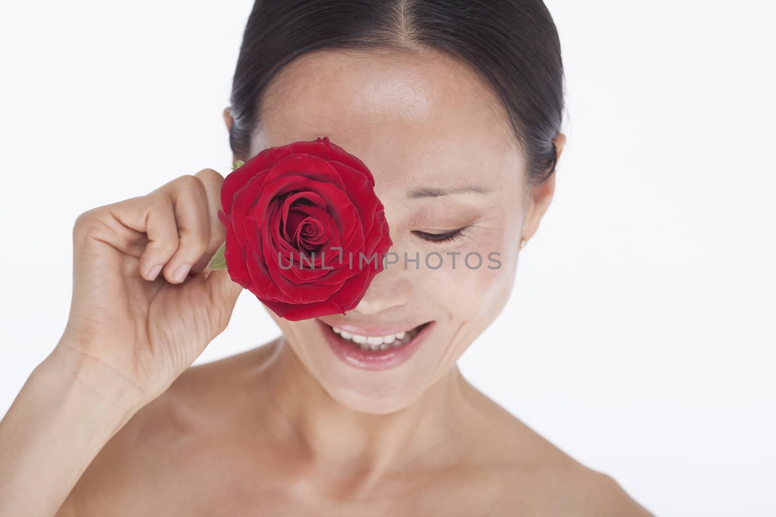 Smiling, beautiful, shirtless woman holding a red rose to her eye, studio shot