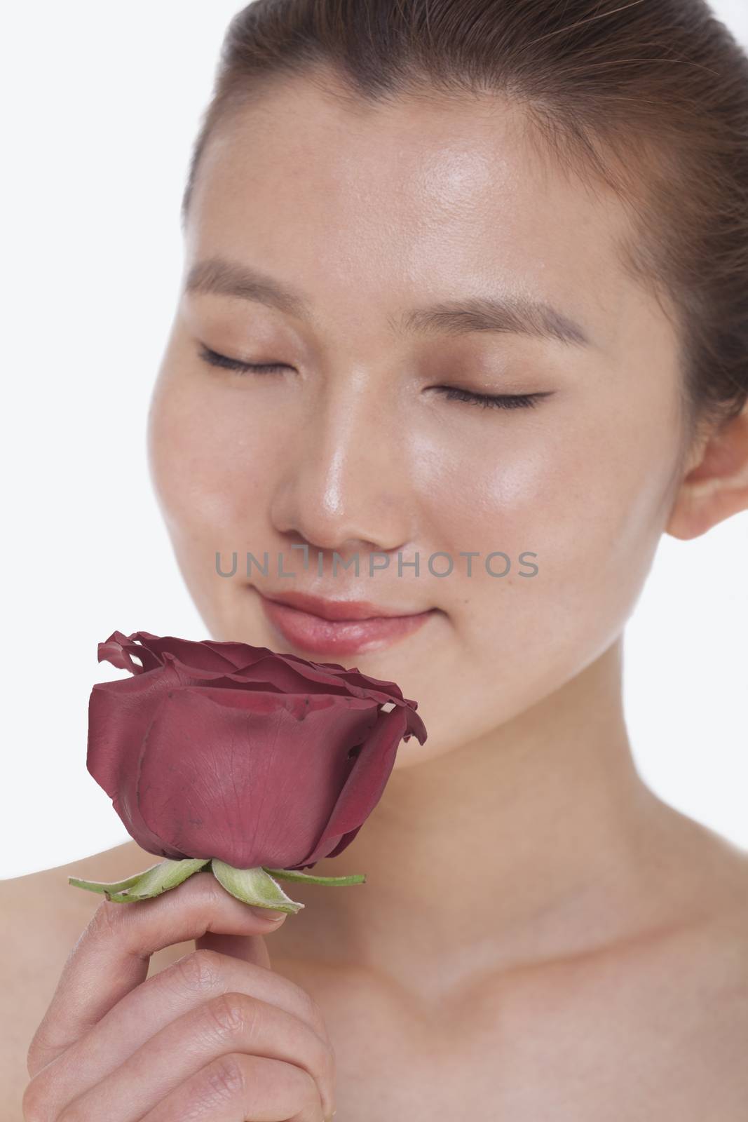 Beautiful young woman with eyes closed smelling a red rose, studio shot by XiXinXing